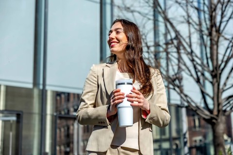 Professional businesswoman looking away and smiling while holding a reusable coffee cup on a sunny