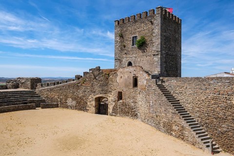 Castle with stone tower and sand courtyard under blue sky, historic and robust, Monsaraz, Évora,