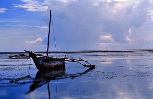 A traditional outrigger boat is quietly lying in the shallow coastal water off Diani Beach. The