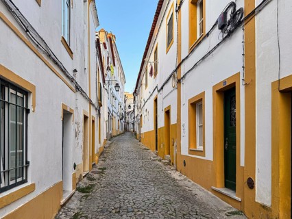 Paved alleyway in a narrow alley between white houses with yellow accents in a quiet old town