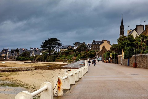 Coast with clouds and historic buildings, people strolling along the beach, Ile de Batz waterfront