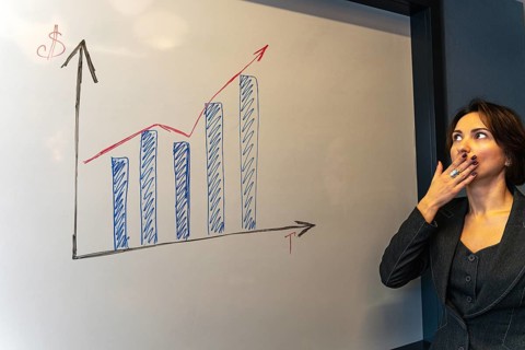 Surprised businesswoman covering mouth while analyzing growth chart at whiteboard