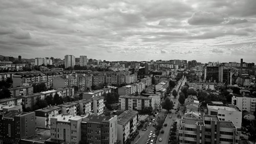 Black and white cityscape with densely packed buildings under a dramatically cloudy sky, Pristina,