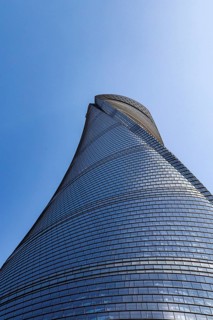 Low-angle view of Shanghai Tower's twisting glass facade spiralling upward into the blue sky,