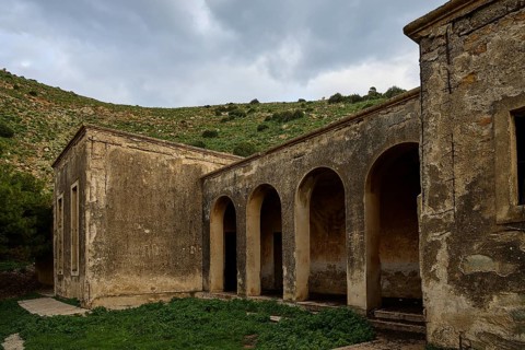 Historic building with arches, surrounded by ruins and green space, in front of a mountain