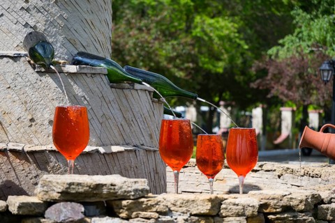 Red glasses under a wine fountain, flowing from bottles across stone, in sunshine, fountain with
