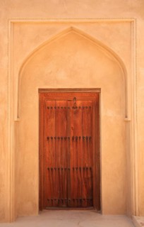 Artfully carved wooden door in an arched beige-wall entrance, courtyard, Fort Nizwa, Ad Dakhiliyah,