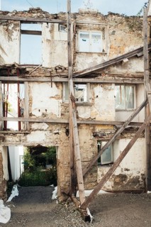 Façade of a heavily damaged building with an integrated historic, medieval city wall that is a