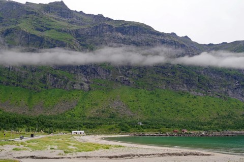 A misty coast with sandy beaches and mountains in the background. Clouds hang low over the