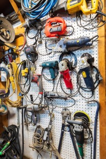 Various electric power tools including drills, circular sanders, jig saw hanging on white pegboard