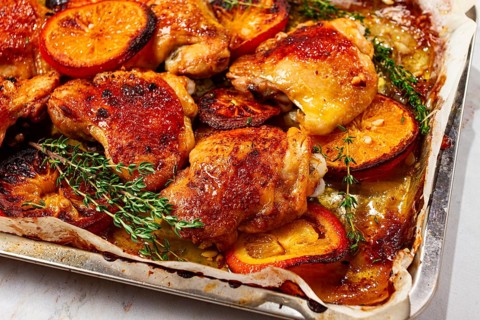 A tray holds cooked chicken thighs topped with orange slices and fresh herbs. The chicken has a