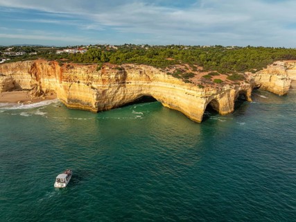Drone view of Benagil Cave cliffs in Algarve, Portugal, with a tourist tour boat, limestone sea