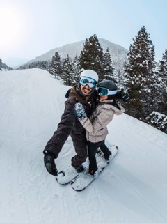 Couple of friends smiling for a selfie while snowboarding down a snowy mountain slope, enjoying an