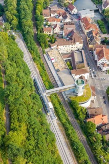 Train crosses bridge, urban environment with dense greenery and building structures, Hermann Hesse
