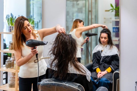 Professional hairdresser blow drying and styling a female client in a modern salon, focusing on