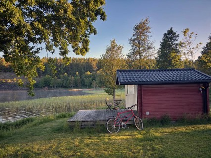 Little red hut with bike on a lake. wooden terrace in quiet, green forest, camping, vacation,
