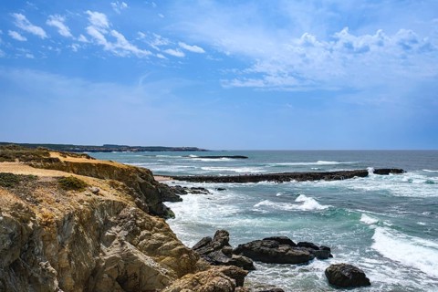 Dramatic coastline with rugged cliffs and undulating ocean under a blue sky, Vila Nova de