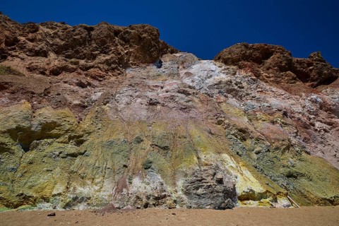 Colourful rock wall under clear blue sky, with various eroded layers, Paliochori beach, Paliochori,