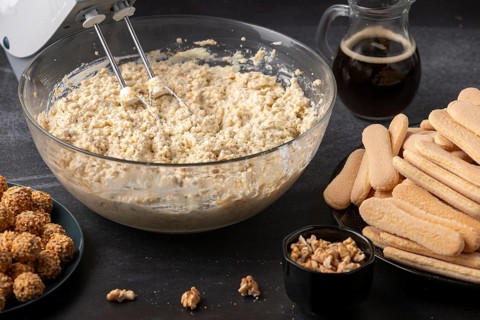 Curd cream is stirred in a glass bowl, followed by sponge cake, coffee and nuts