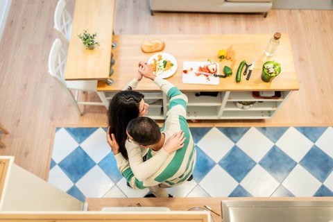 Young couple embracing and dancing on a bright kitchen island while preparing a healthy vegetable