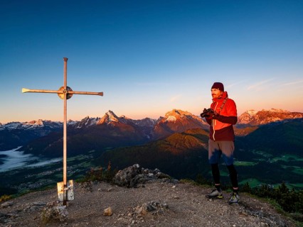 Mountaineers with camera at the Rauher Kopf summit cross at sunrise, in the background the