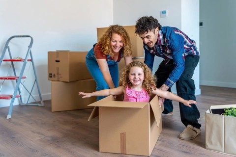 Parents playfully pushing their smiling daughter in a cardboard box on the floor of their new