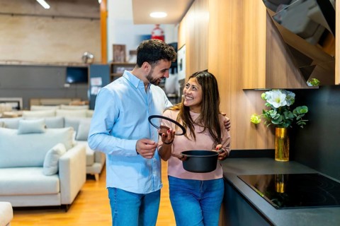 Happy young couple looking at products and discussing options while choosing kitchen appliances and