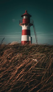 A lighthouse rises above grassy fields at an atmospheric dusk, Grisetaodde lighthouse, Neno Sound