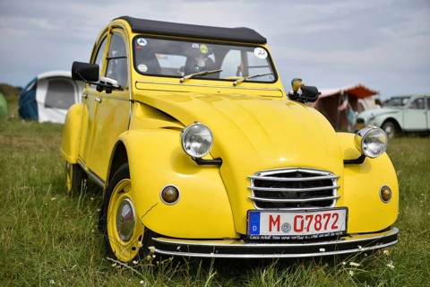A yellow Citroën 2CV stands in a meadow surrounded by tents, radiates classic charm, Citroën 2CV at