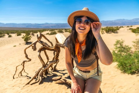 Woman smiling and adjusting sunglasses while sitting on mesquite flat sand dunes in death valley