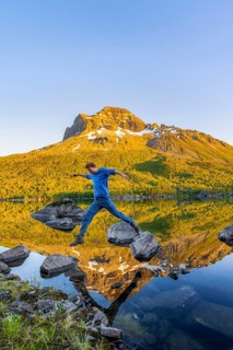 Young man jumping from stone to stone in water, picturesque mountain landscape in the Innerdalen