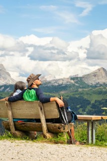 Caucasian couple hikers sit on hand made wooden bench, admiring the majestic Dolomites mountain