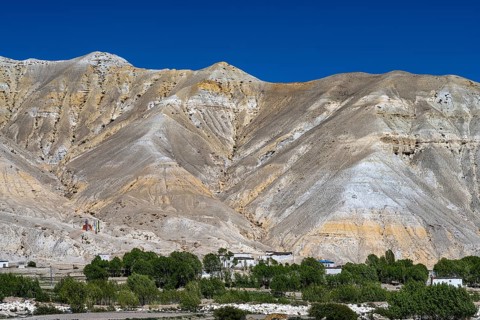 Small settlement and cultivated fields in front of mountainous landscape, erosion landscape near Lo