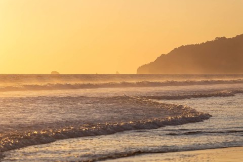The low sun's golden light illuminates the ocean spray on Carate Beach, with views of Corcovado NP