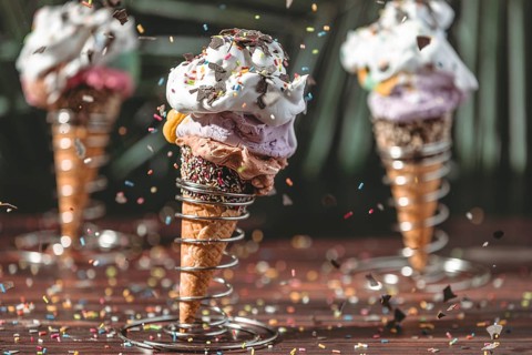 Sprinkles fall on colorful ice cream in waffles in metal holders with cream