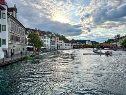 Riverfront building in evening sun with reflections in water and cloudy sky, Lucerne, Switzerland