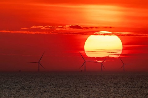 Dramatic sunset over the sea, wind turbines and wind turbines on the horizon, streaks of clouds,