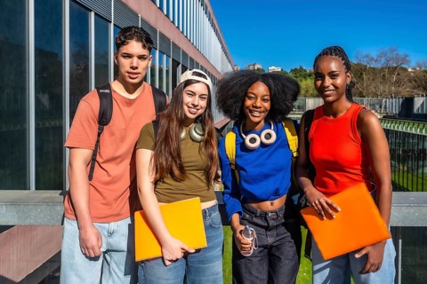 Diverse group of smiling young students standing on a modern university campus, wearing backpacks