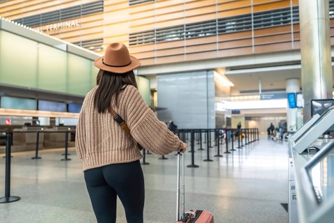 Young woman walks through a bright modern airport terminal pulling a suitcase, arriving or