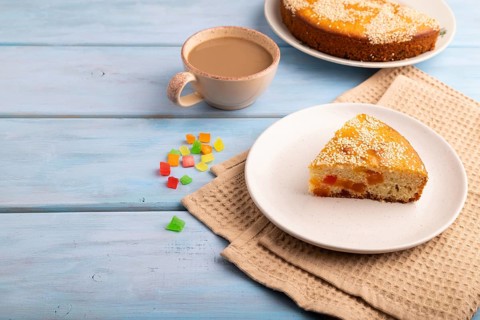 Pie with candied fruit, cup of coffee, on blue wooden background with beige textile, copy space,