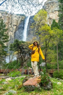 Woman wearing yellow raincoat standing on a rock, admiring the powerful bridalveil fall and lush