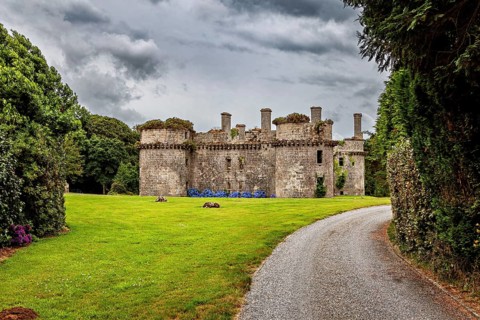 View of an old ruin with round towers from a curved path surrounded by greenery, The ruins of the