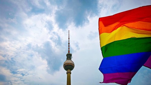 The Berlin TV Tower rises into the sky while a rainbow flag blows in the wind and radiates pride,