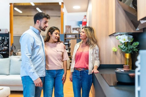 Young couple talking with a female sales consultant in a modern kitchen showroom, exploring