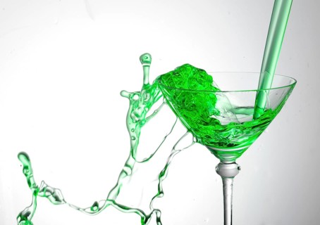 A powerful flood of green liquid pours into a cocktail glass and spills over, studio shot against a