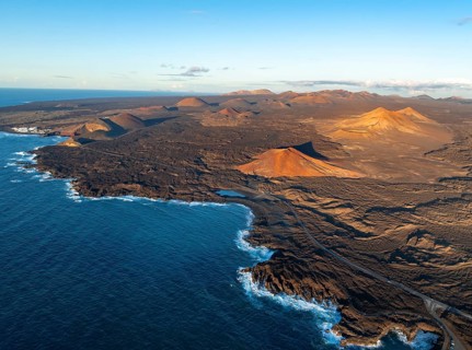 Coast with lava fields, volcanic landscape near Los Hervideros with red volcano Montaña Bermeja, in
