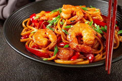 Udon stir-fry shrimp noodles with red bell pepper and green onion, served in a black bowl, with
