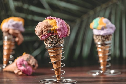 Three ice cream cones with colorful ice cream set up in a tropical setting