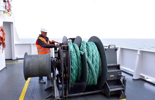 A worker operates a machine on a ship deck with a view of the sea, worker on a tow winch on a