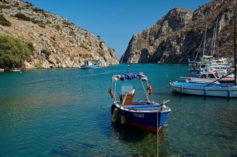 A boat is anchored in clear, blue water between rocky cliffs, Rina, harbour, Vathi, Vathys,